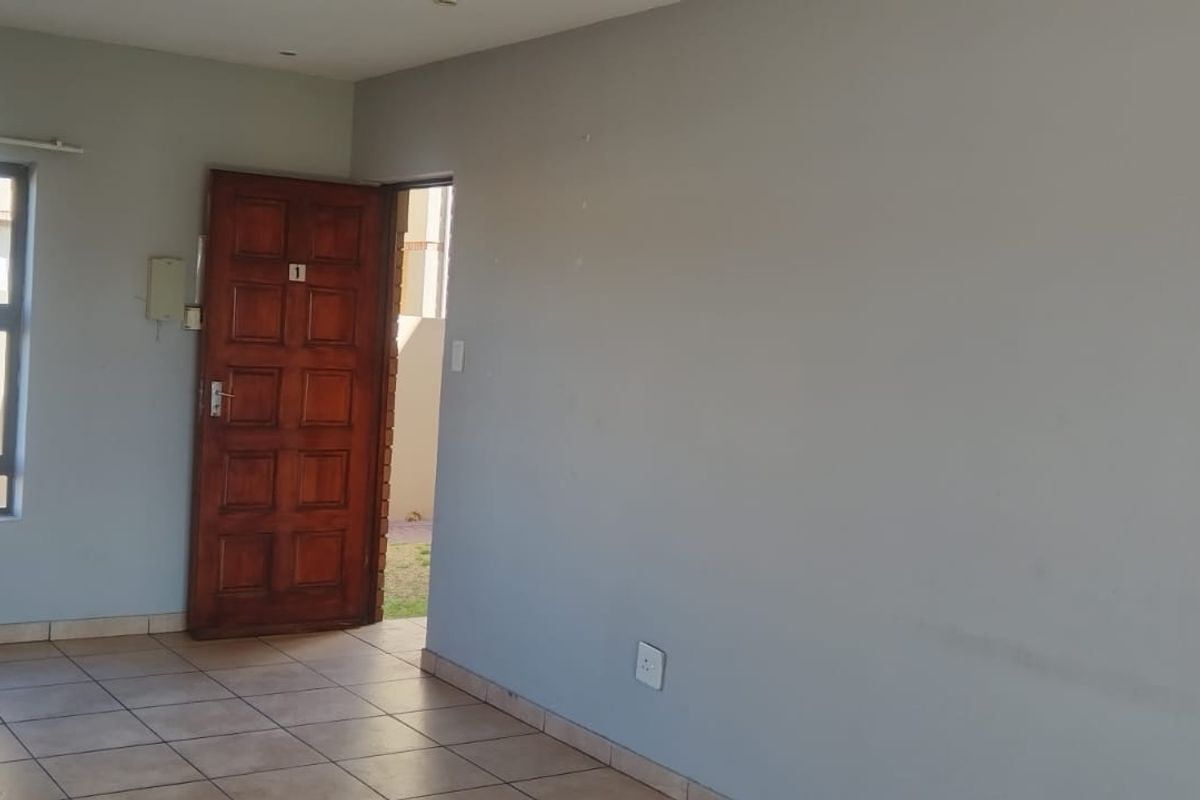 An empty living area featuring neutral wall paint, tiled flooring, and a timber entrance door with natural light from the window.
