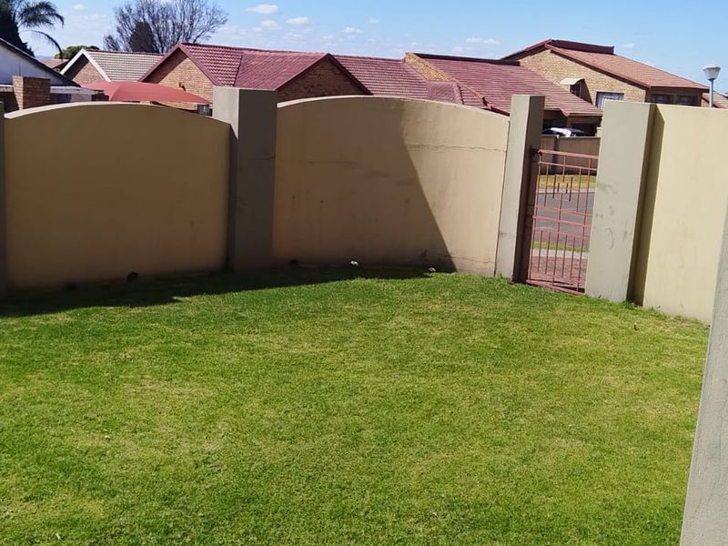 A private garden area featuring a well-maintained lawn enclosed by a perimeter wall with a secure metal pedestrian gate.