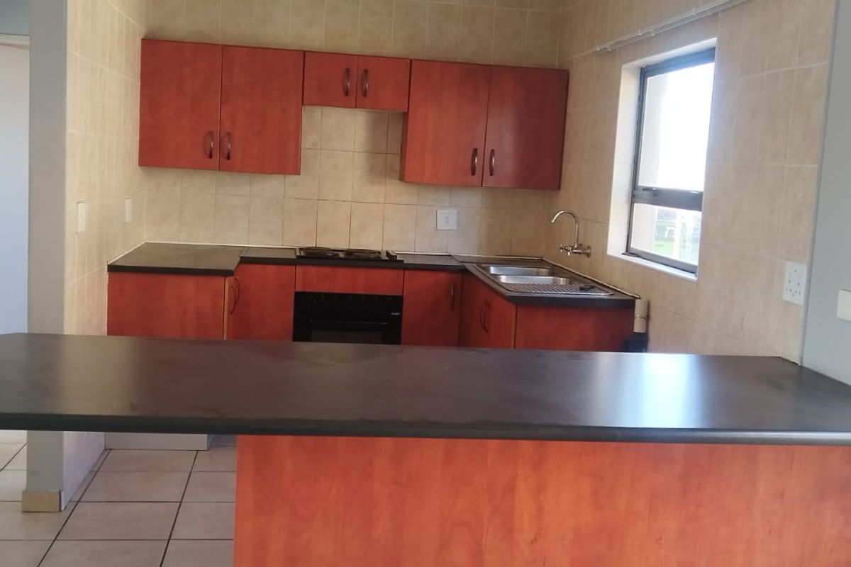 A functional kitchen featuring wood-finish cabinetry, dark laminate countertops, a breakfast bar, and built-in cooking appliances with tiled splashbacks.