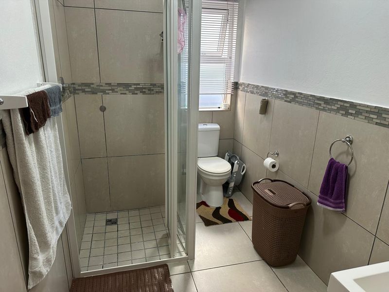 A functional bathroom featuring a glass-enclosed shower, a standard toilet, and neutral wall and floor tiling with a decorative mosaic border.
