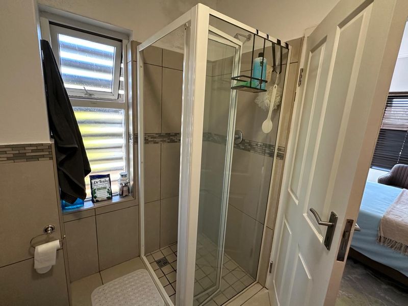 A functional bathroom featuring a glass-enclosed shower, neutral wall tiling with decorative accents, and a window for natural light.