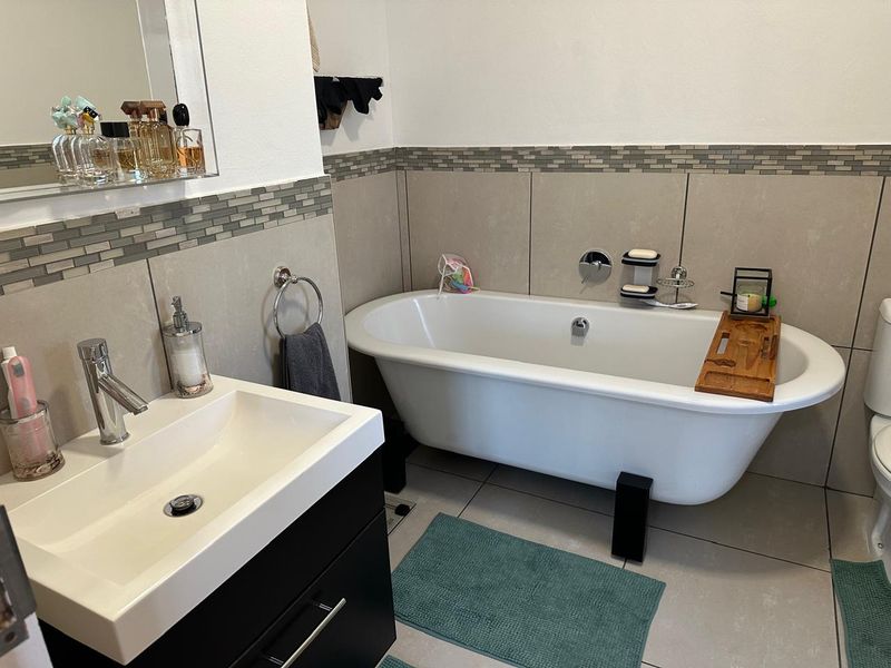 Modern bathroom featuring a freestanding bathtub, vanity cabinet with basin, and neutral wall tiling with a decorative mosaic border.