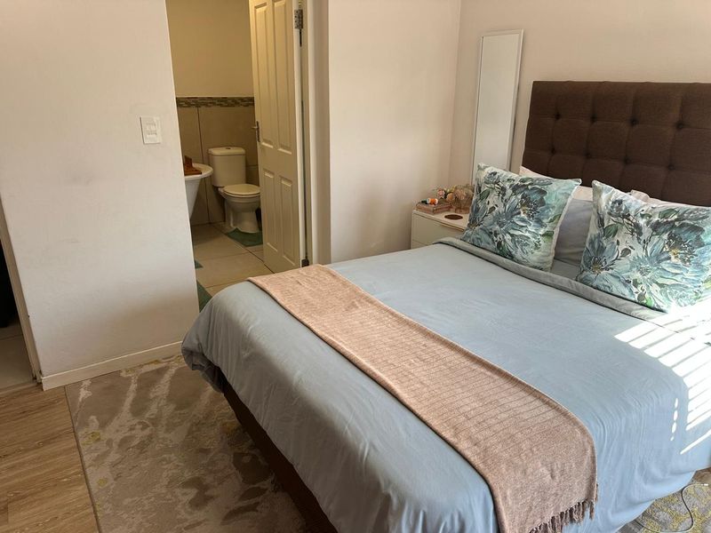 A well-maintained bedroom featuring laminate flooring and direct access to an en-suite bathroom with tiled finishes.