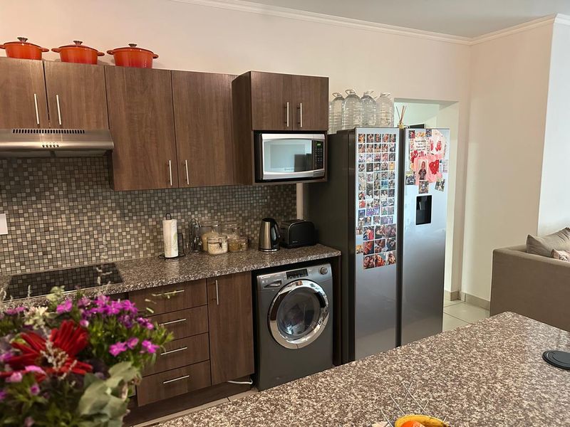 A functional kitchen featuring dark wood cabinetry, granite countertops, a mosaic tile backsplash, and integrated appliances including a washing machine and microwave.