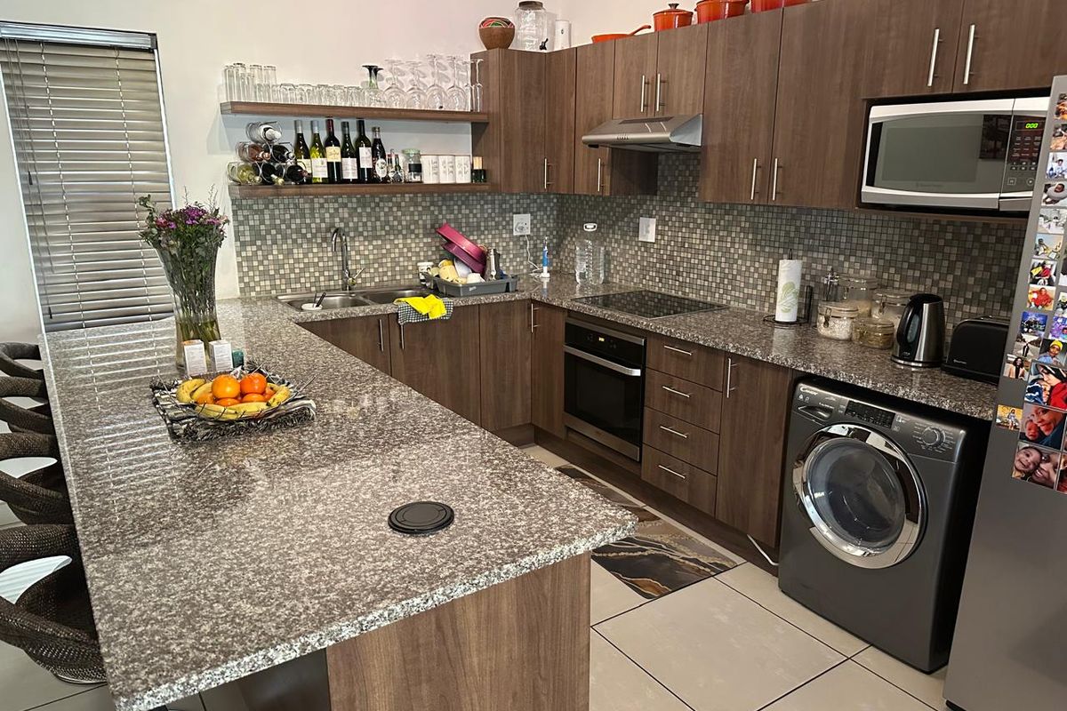 Modern kitchen featuring granite countertops, mosaic tile backsplash, built-in oven, hob, extractor fan, and integrated laundry appliance with ample cabinetry.