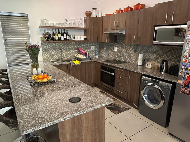 Modern kitchen featuring granite countertops, mosaic tile backsplash, built-in oven, hob, extractor fan, and integrated laundry appliance with ample cabinetry.