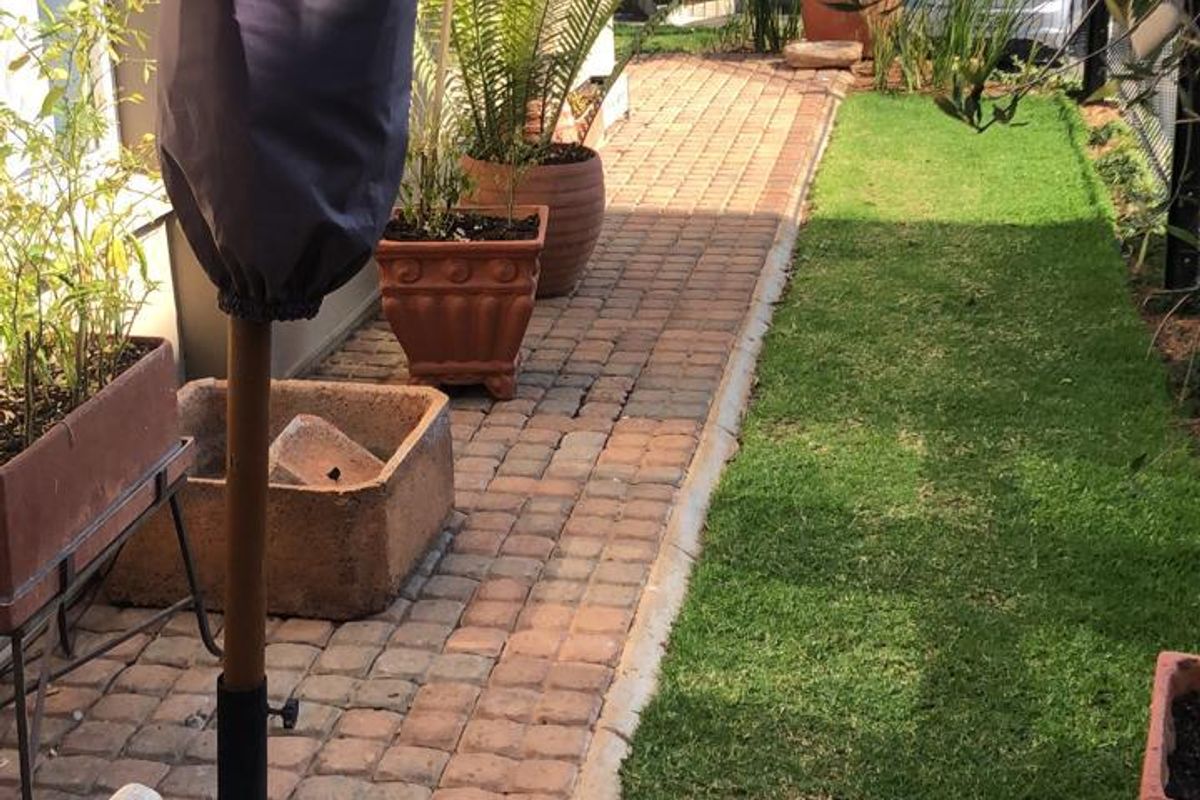 A well-maintained rear garden area featuring brick paving, a neat lawn, and secure perimeter fencing.