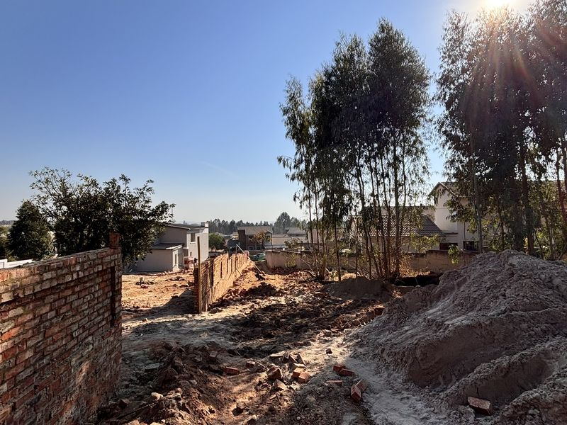 An undeveloped residential plot featuring a brick boundary wall and natural landscaping, currently undergoing site preparation or construction work.