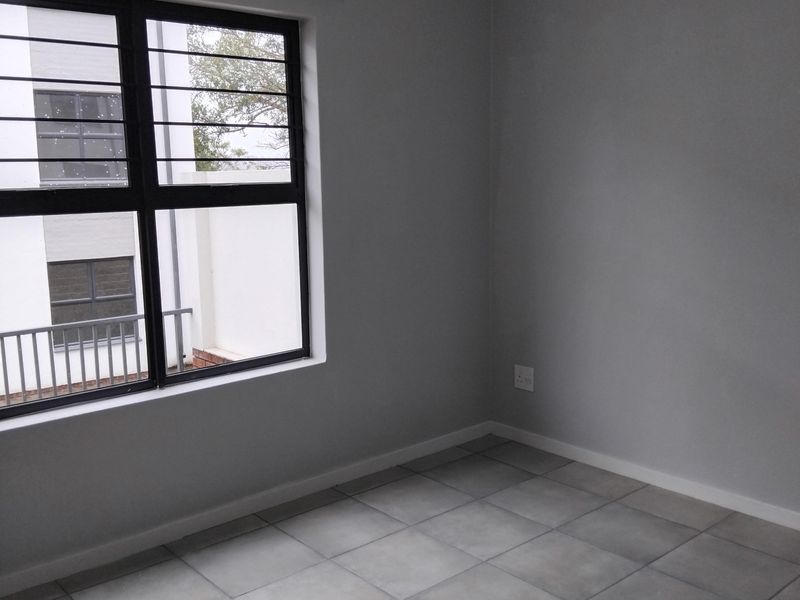 A clean, empty bedroom featuring neutral grey tiled flooring, freshly painted walls, and a window fitted with security bars.
