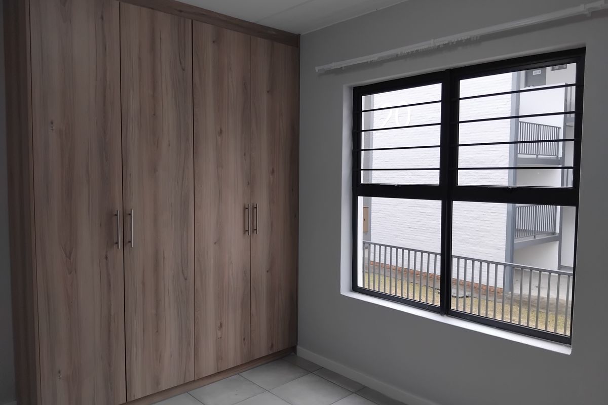 A clean, empty bedroom featuring modern wood-finish built-in cupboards, tiled flooring, and a window fitted with security bars.