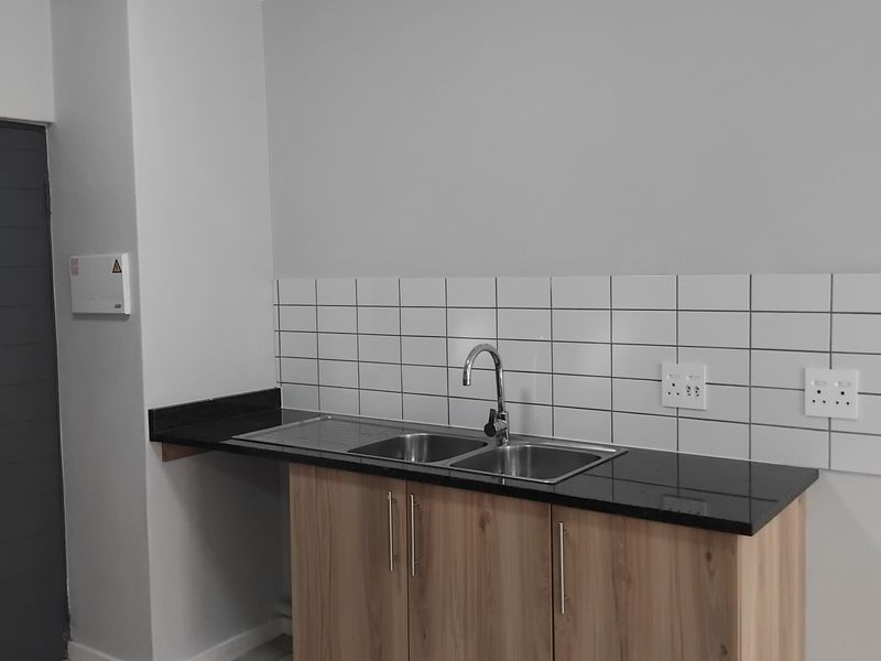 A clean, modern kitchen area featuring light wood cabinetry, a black granite countertop, stainless steel sink, and a white subway tile backsplash.