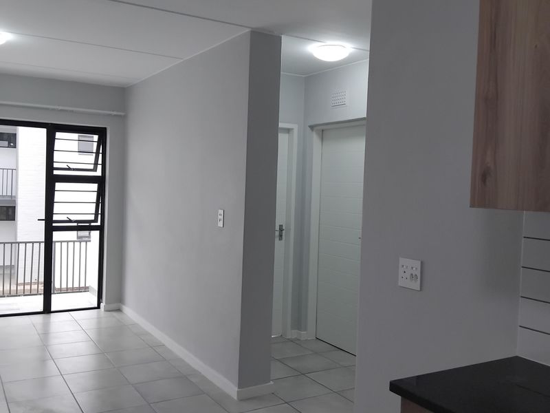 An open-plan living area featuring neutral tiled flooring, modern kitchen cabinetry with dark countertops, and direct access to a balcony through sliding glass doors.
