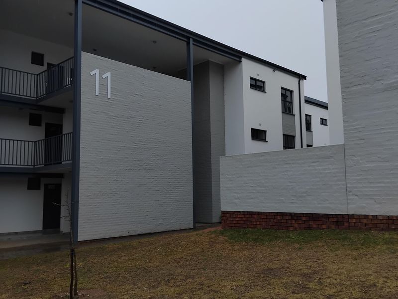 Exterior view of a modern apartment complex building featuring painted brick walls, metal balcony railings, and covered walkways.