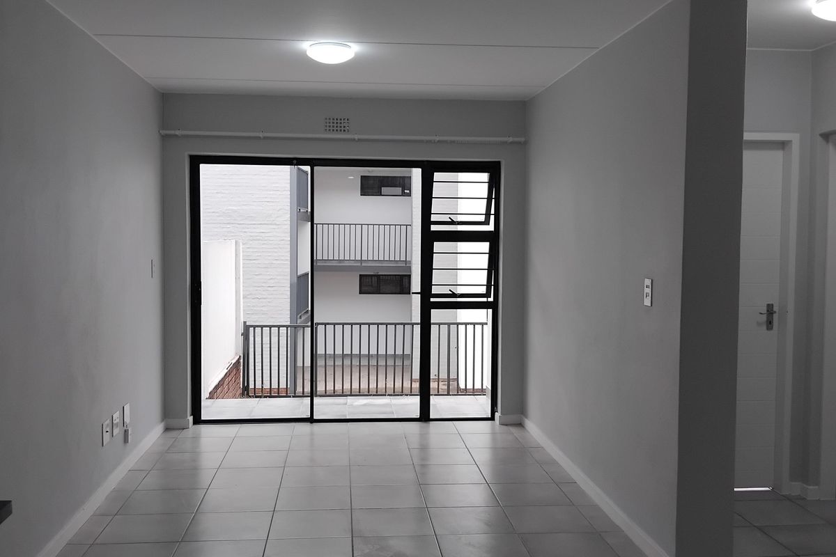 An empty, neutrally painted living area featuring tiled flooring and a large sliding glass door providing access to an outdoor balcony.