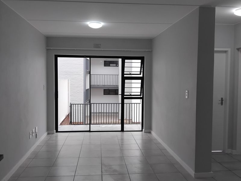 An empty, neutrally painted living area featuring tiled flooring and a large sliding glass door providing access to an outdoor balcony.