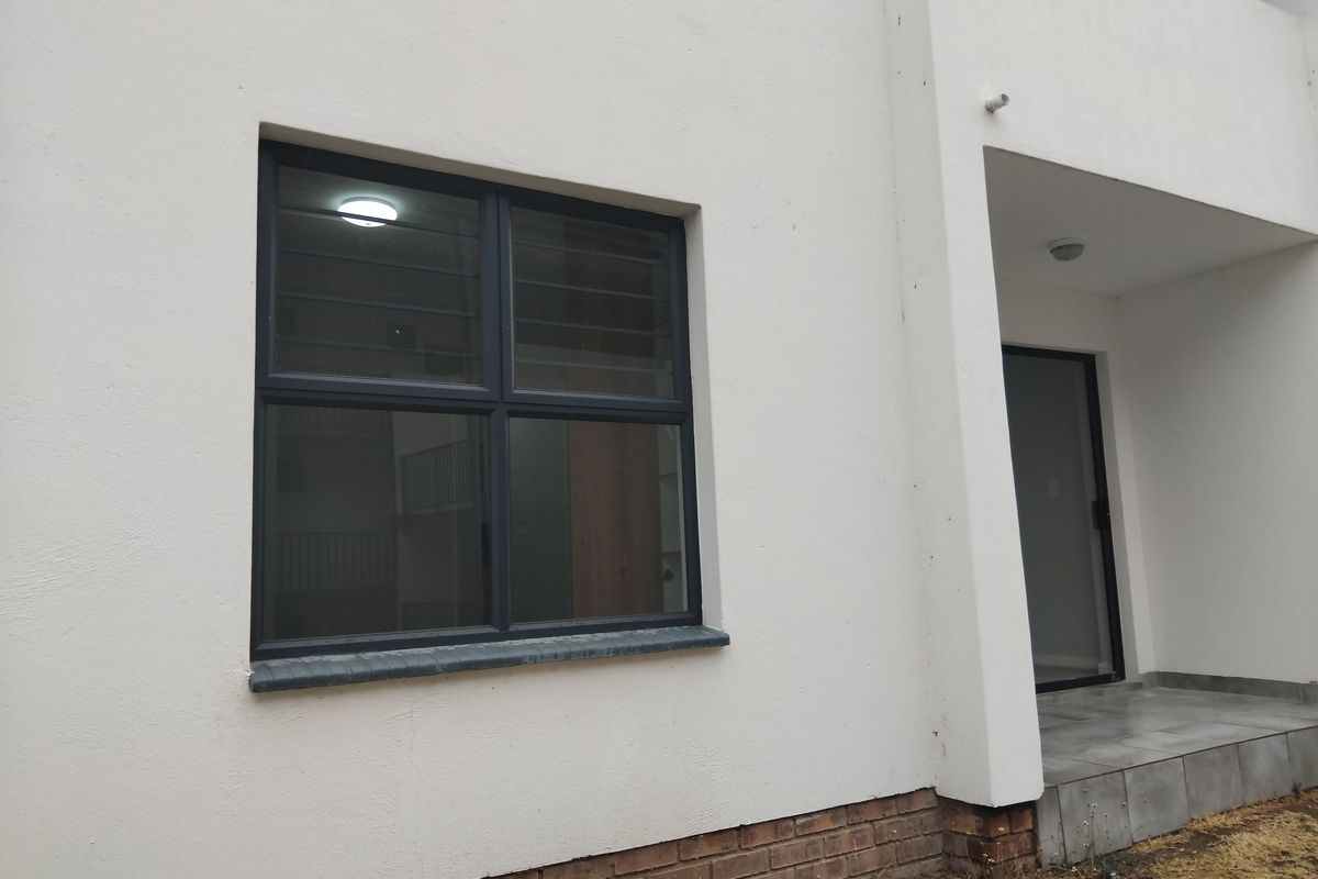 Exterior view of an apartment featuring dark aluminium window frames, a small tiled patio area, and a brick base course.