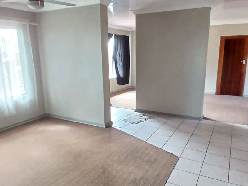 An empty open-plan living area featuring a mix of carpeted and tiled flooring, coved cornicing, and a ceiling fan.
