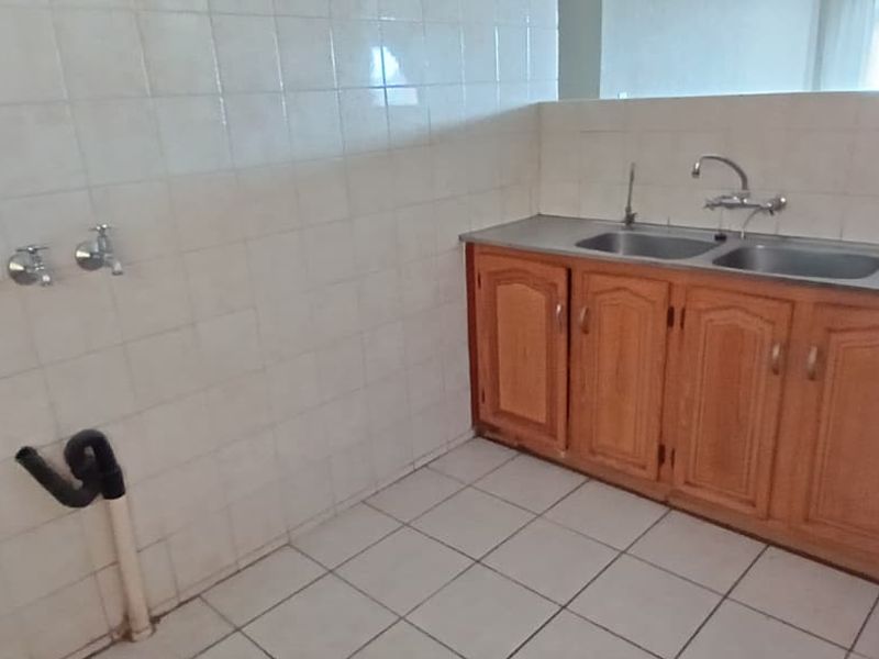 A functional laundry area featuring a double stainless steel sink, wooden cabinetry, and tiled splashback with dedicated plumbing connections for appliances.