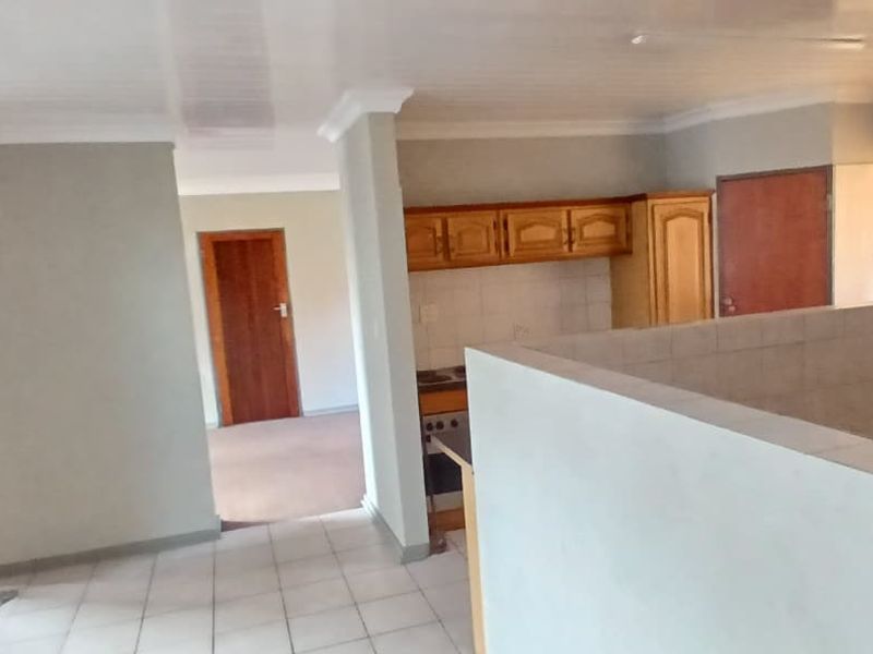 Open plan living area featuring tiled floors, coved ceilings, and a functional kitchen with built-in wooden cabinetry and stove.