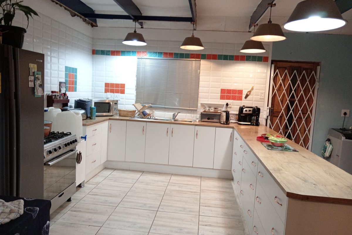 Spacious kitchen featuring a large island, gas stove, tiled backsplash, and exposed ceiling beams, offering a functional layout with ample storage cabinetry.