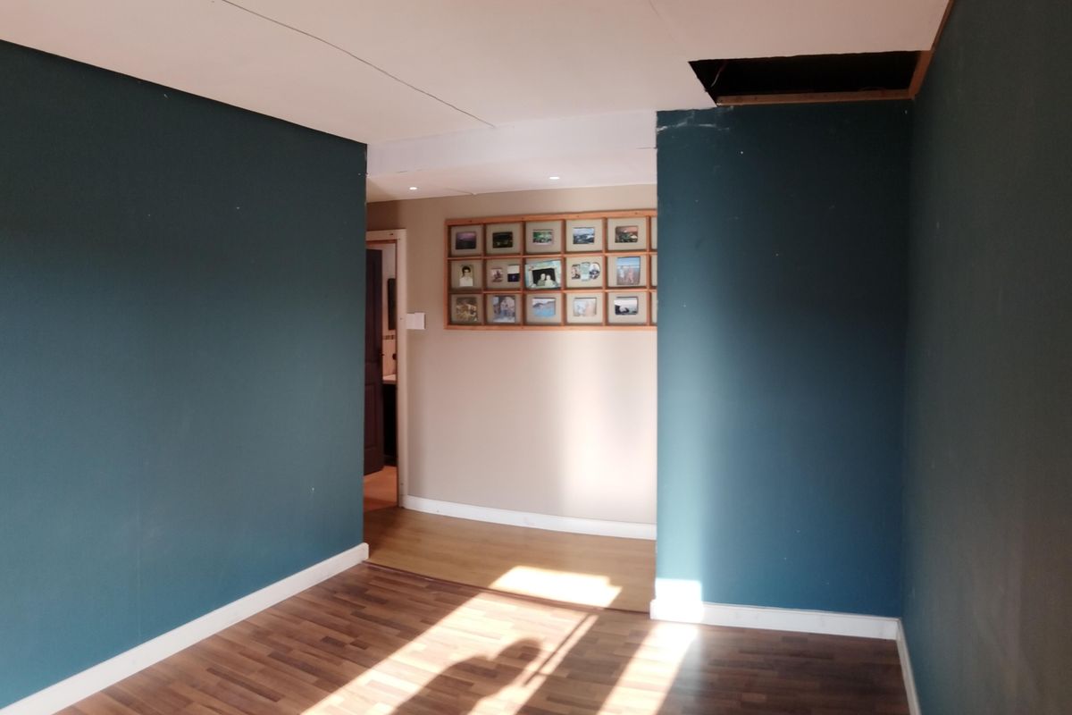 An empty living area featuring dark teal walls, laminate flooring, and a visible hole in the ceiling requiring repair.