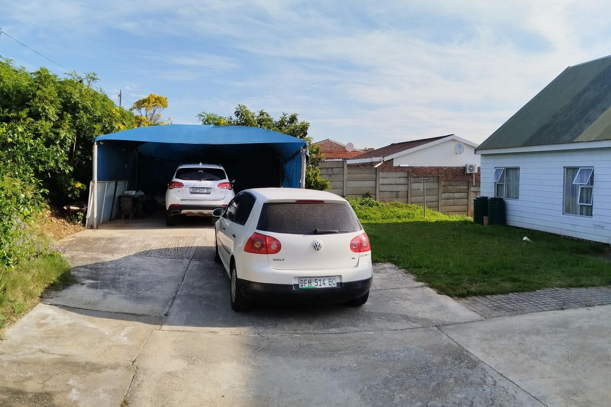 Rear exterior view featuring a concrete driveway, a covered carport structure, and a lawn area enclosed by a precast concrete boundary wall.