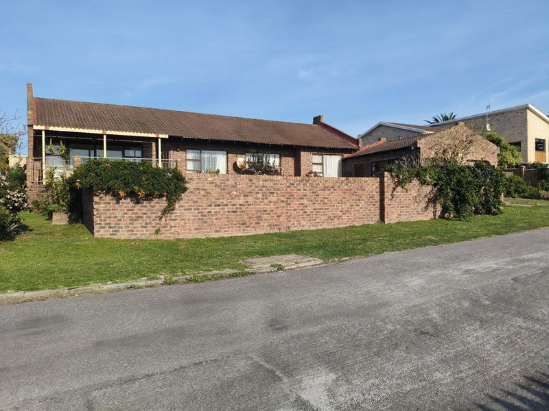 Front view of a single-story house featuring a brick boundary wall, tiled roof, and an attached garage with a covered patio area.