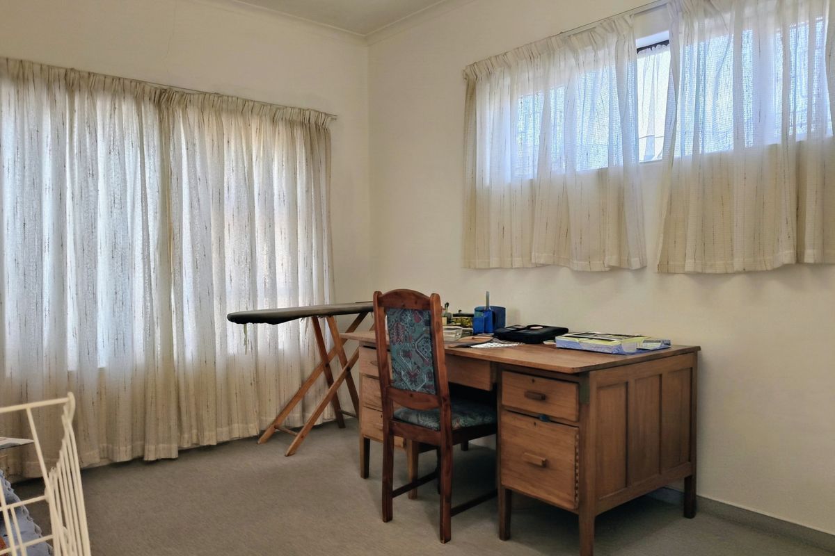 A bedroom featuring carpeted flooring and dual window treatments, currently utilized as a home office space.