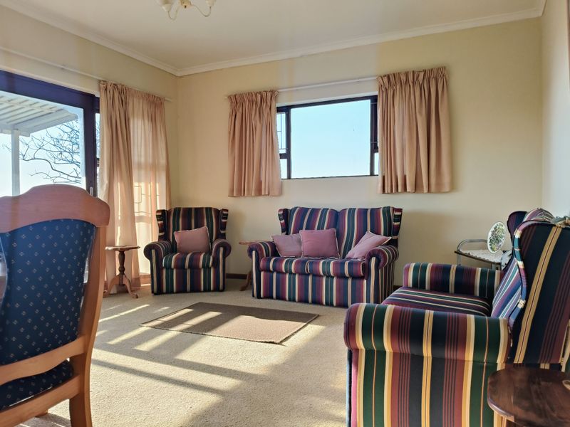 A sunlit living room featuring carpeted flooring, large windows, and a sliding glass door providing access to the outdoor area.