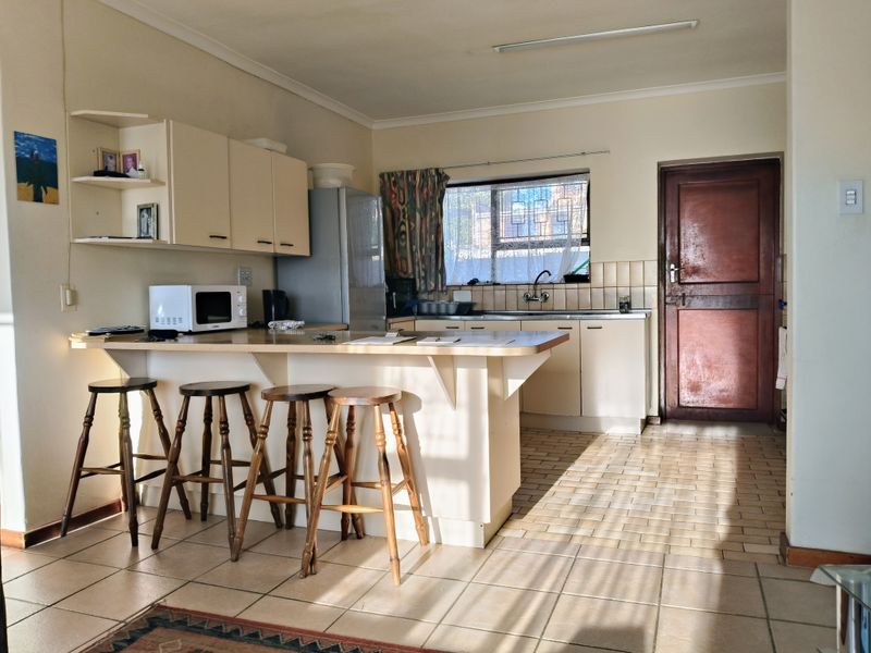 A functional kitchen featuring built-in cabinetry, a breakfast bar, tiled flooring, and a tiled backsplash, offering a practical layout with natural light.