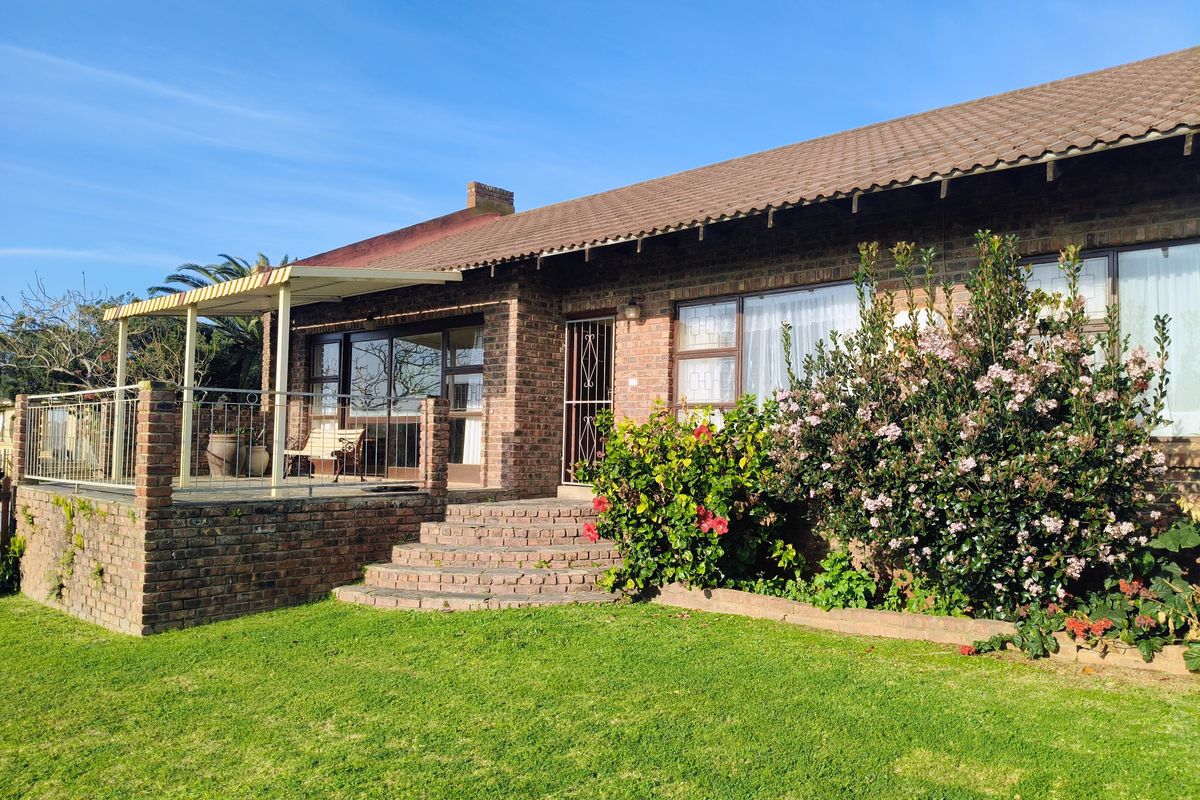 Rear view of a brick house featuring a raised patio with metal railings, an awning, and direct access to the garden via sliding doors.
