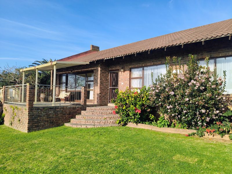 Rear view of a brick house featuring a raised patio with metal railings, an awning, and direct access to the garden via sliding doors.