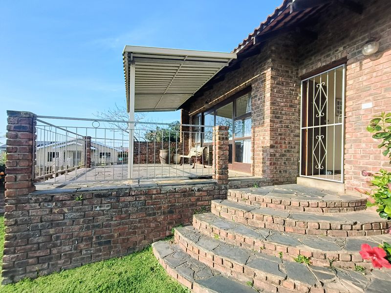 A brick-built patio area featuring stone paving, a metal awning for shade, and curved brick steps leading to the garden.