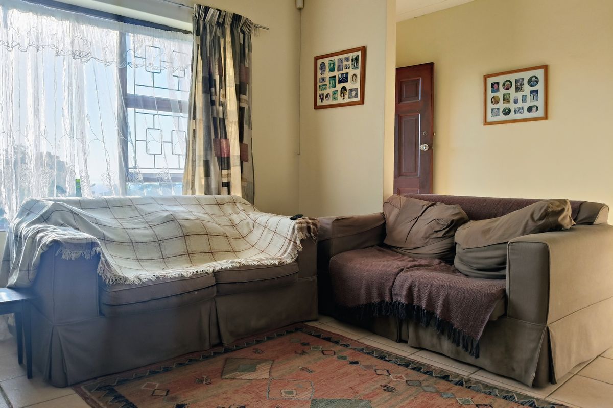 A living room featuring tiled flooring and a large window with security bars, providing natural light to the space.