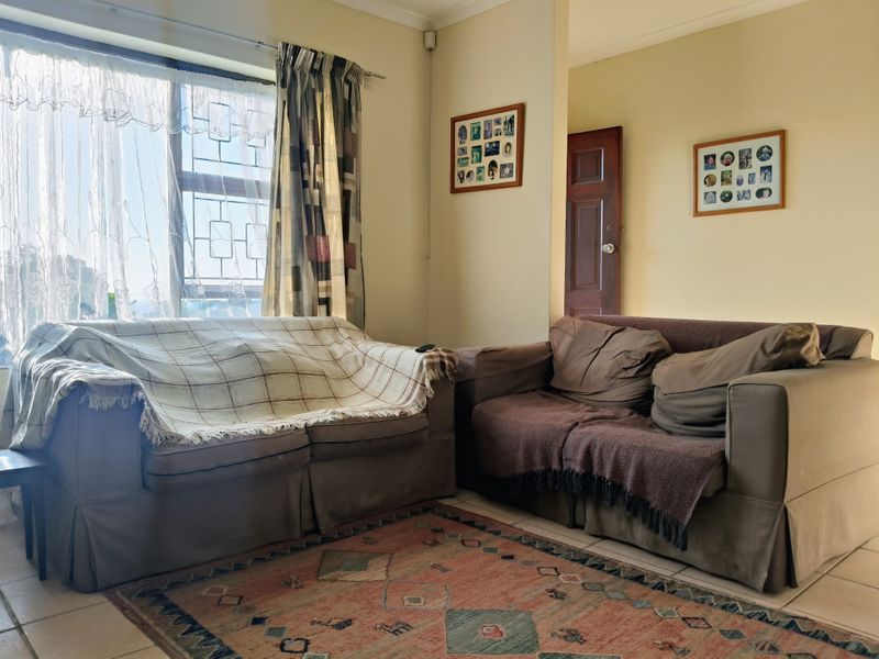 A living room featuring tiled flooring and a large window with security bars, providing natural light to the space.