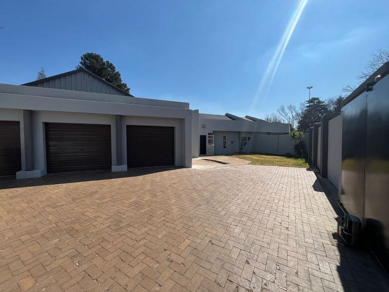 Spacious front exterior featuring a triple garage with roller doors and a large paved driveway, enclosed by a secure boundary wall.