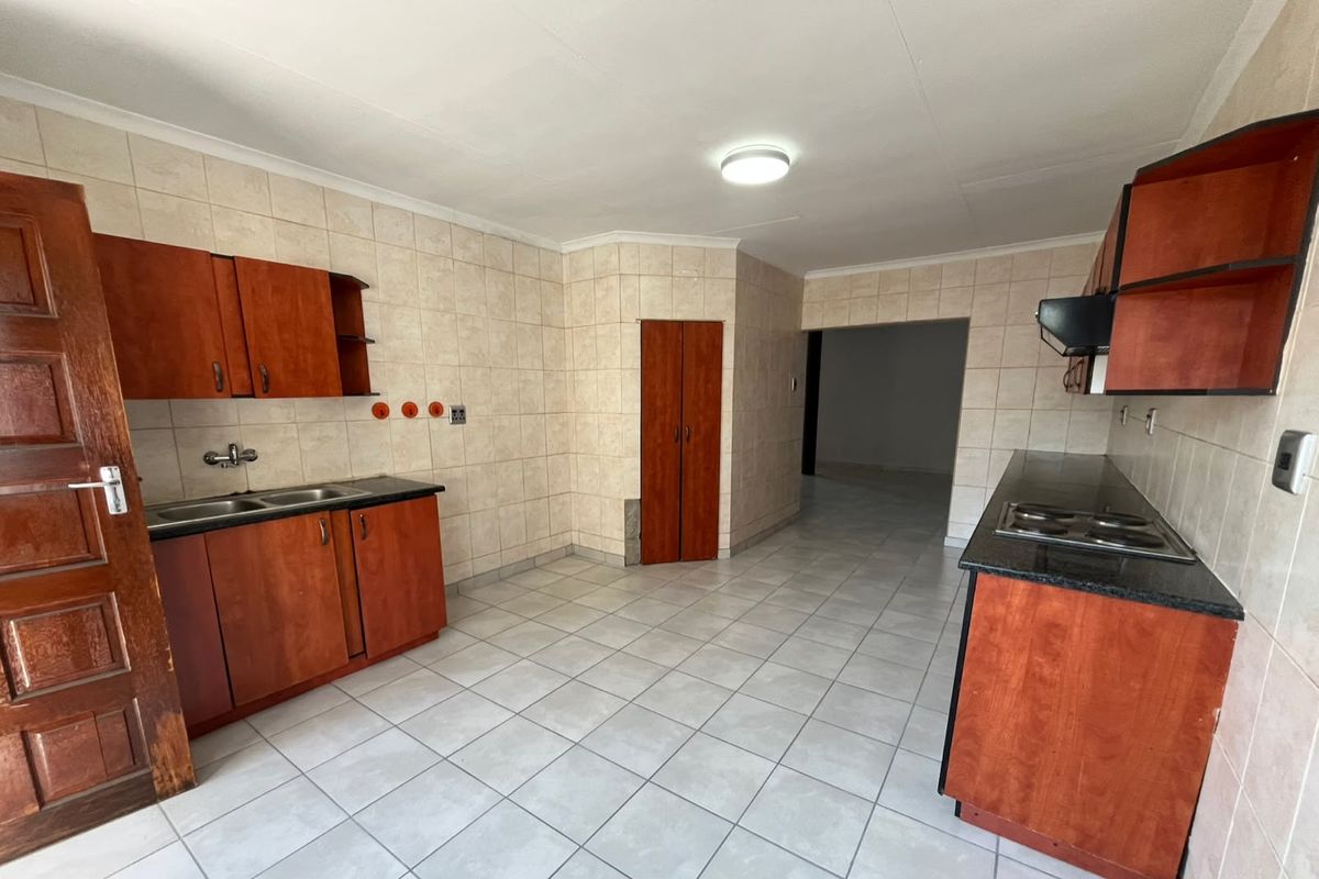 A functional kitchen featuring built-in wooden cabinetry, granite countertops, an electric hob with extractor, and neutral tiled finishes throughout.