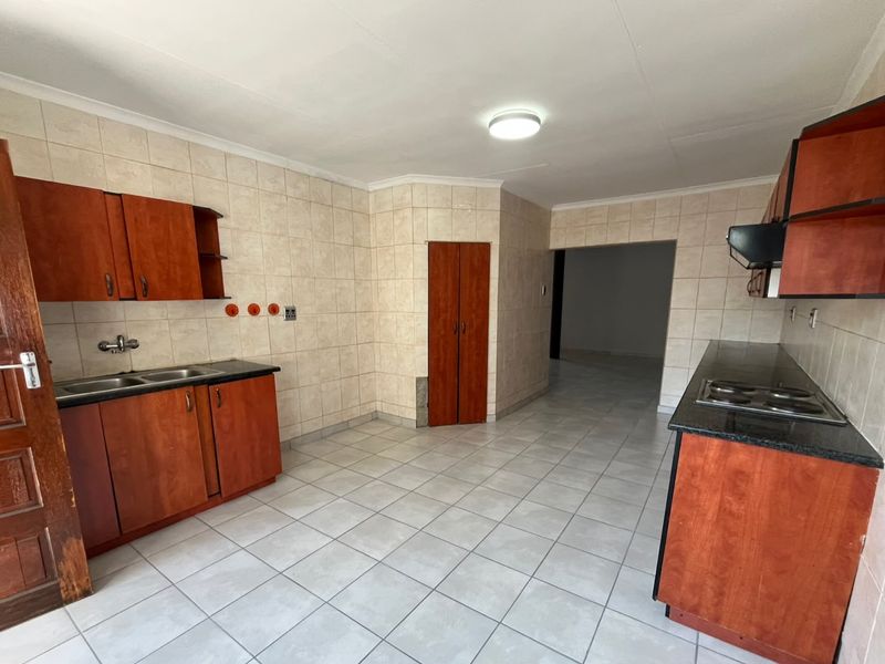 A functional kitchen featuring built-in wooden cabinetry, granite countertops, an electric hob with extractor, and neutral tiled finishes throughout.