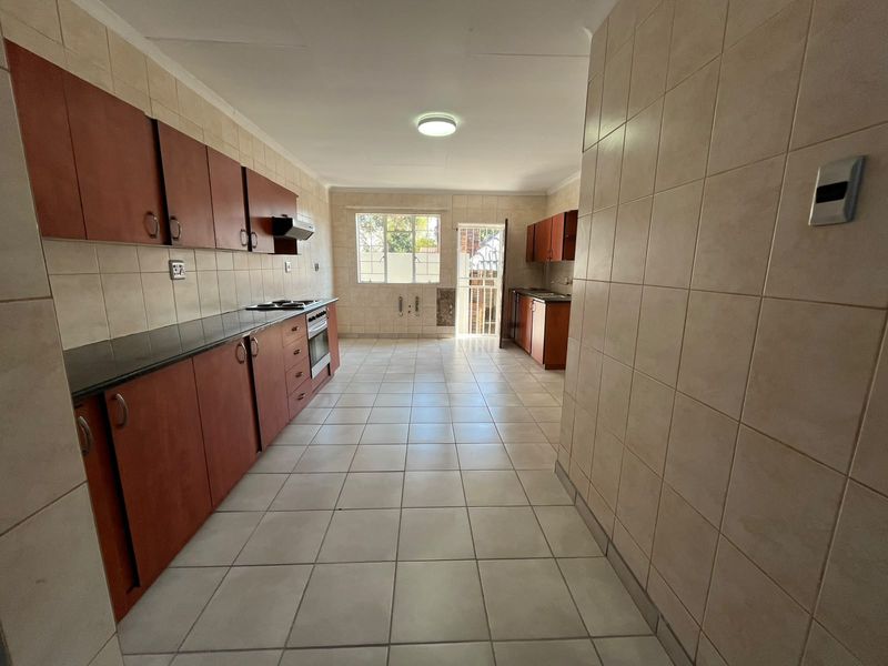 A spacious, empty kitchen featuring built-in cabinetry, granite countertops, a built-in oven, and tiled finishes throughout, offering a functional layout for renovation.