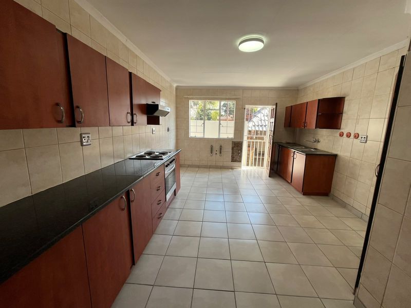 A spacious, empty kitchen featuring dark wood cabinetry, granite countertops, built-in oven and hob, and neutral tiled flooring throughout.