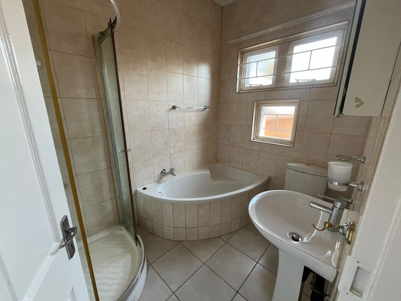 A functional bathroom featuring a corner bathtub, separate shower enclosure, pedestal sink, and toilet with neutral wall and floor tiling.