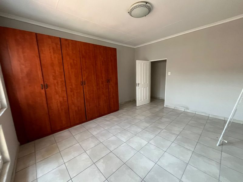 A spacious, empty bedroom featuring neutral tiled flooring, built-in wooden cupboards, and a simple ceiling light fixture.