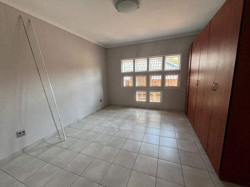 A vacant bedroom featuring tiled flooring, built-in wooden cupboards, and unique grid-pattern windows, offering a clean and functional space.