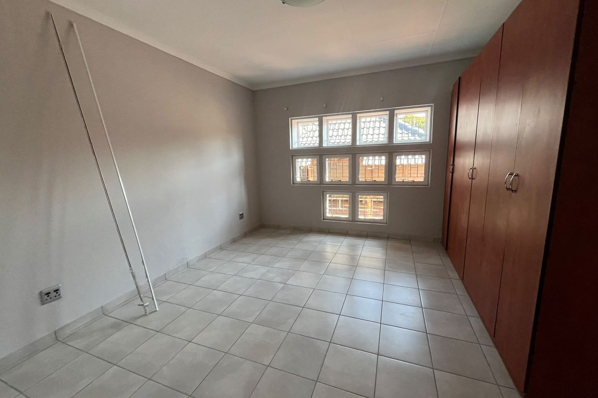 A vacant bedroom featuring tiled flooring, built-in wooden cupboards, and unique grid-pattern windows, offering a clean and functional space.