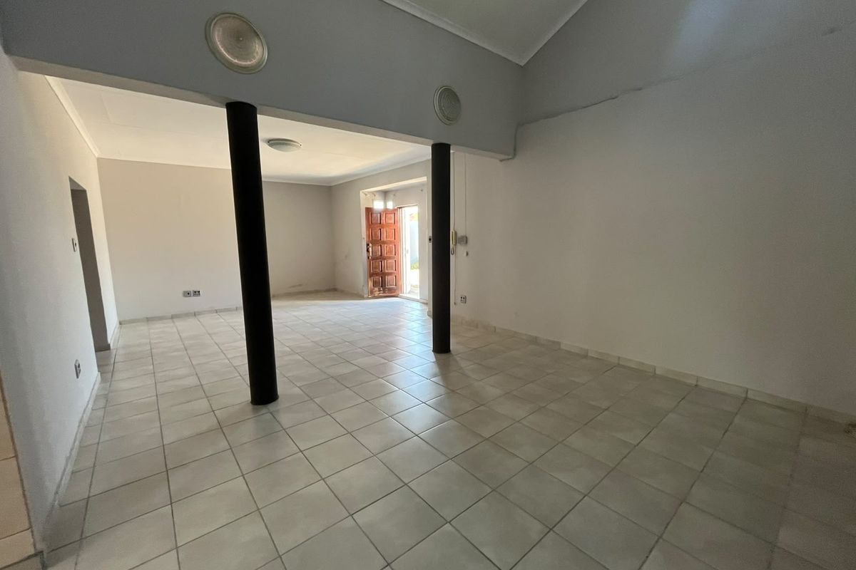 Spacious, open-plan living area featuring neutral tiled flooring, structural support columns, and a timber entrance door, offering a blank canvas for interior design.