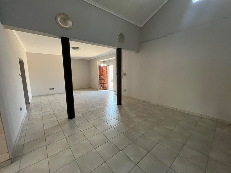 Spacious, open-plan living area featuring neutral tiled flooring, structural support columns, and a timber entrance door, offering a blank canvas for interior design.
