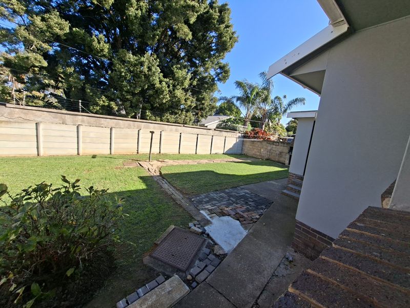 A rear garden area featuring a lawn, paved walkway, and precast concrete boundary wall with electric fencing.