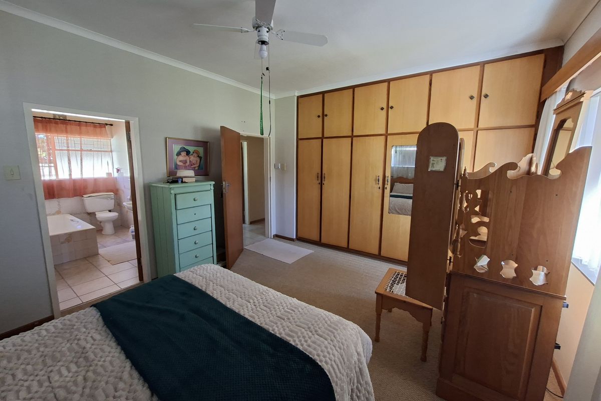 Spacious bedroom featuring extensive built-in wooden cupboards, a ceiling fan, and direct access to an en-suite bathroom with tiled flooring.