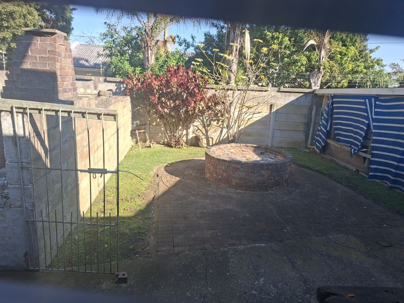 Rear garden area featuring a brick fire pit, paved patio, and outdoor fireplace, enclosed by boundary walls.