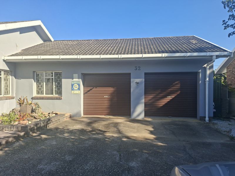 Front view of the property featuring a double garage with roller doors, tiled roof, and a small brick planter area.